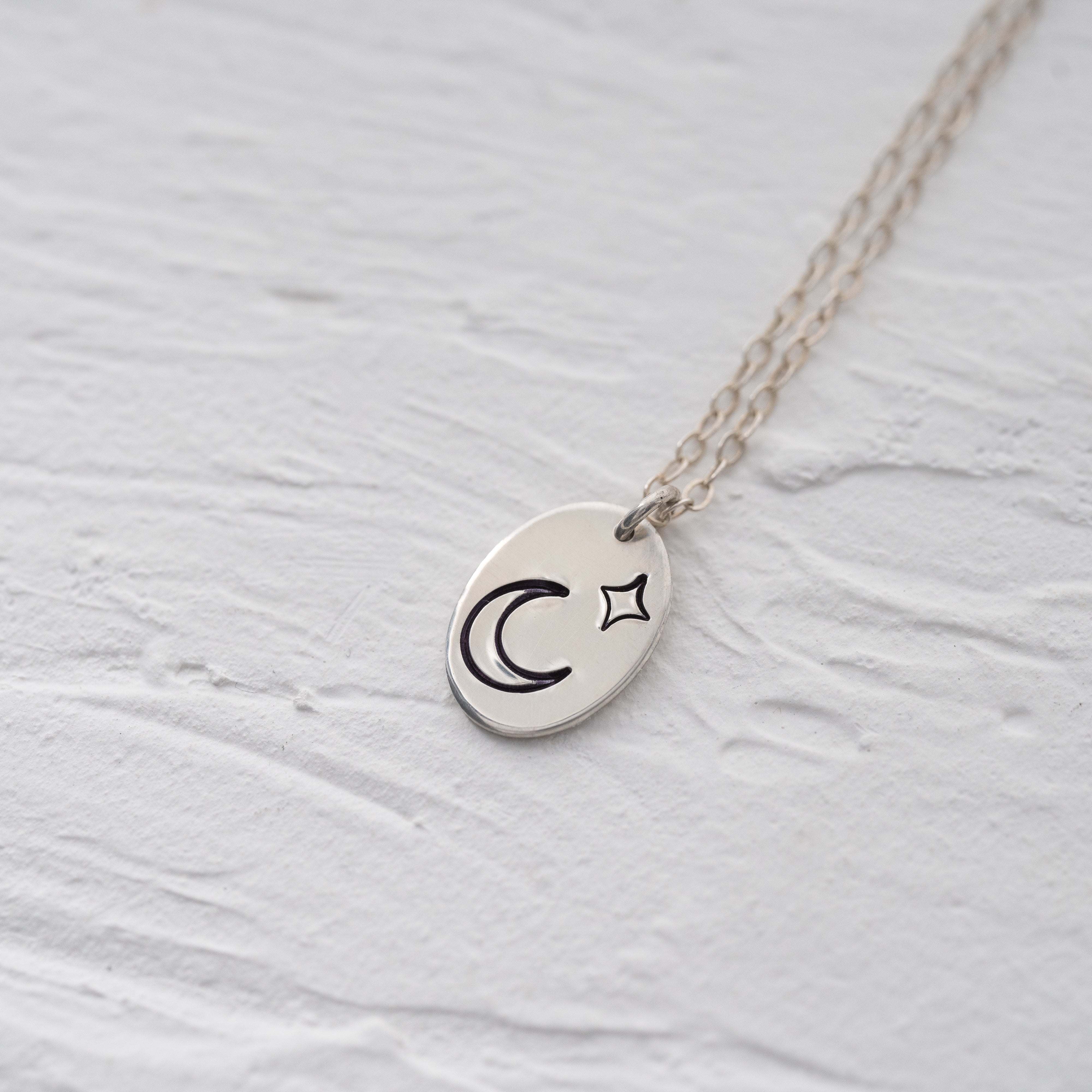 Silver oval shaped pendant with a moon and a star above